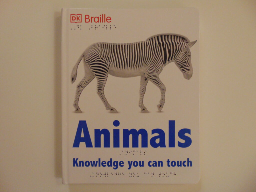 Front cover with a white background, “DK” with an outline of a book around it and “Braille” in red print and the braille translation underneath in the top left corner, a black and white stiped zebra with tactile white stripes is in the center, underneath the zebra is the large print word “Animals” in blue with the braille translation underneath, under that is “Knowledge you can touch” in print in blue with the braille translation underneath