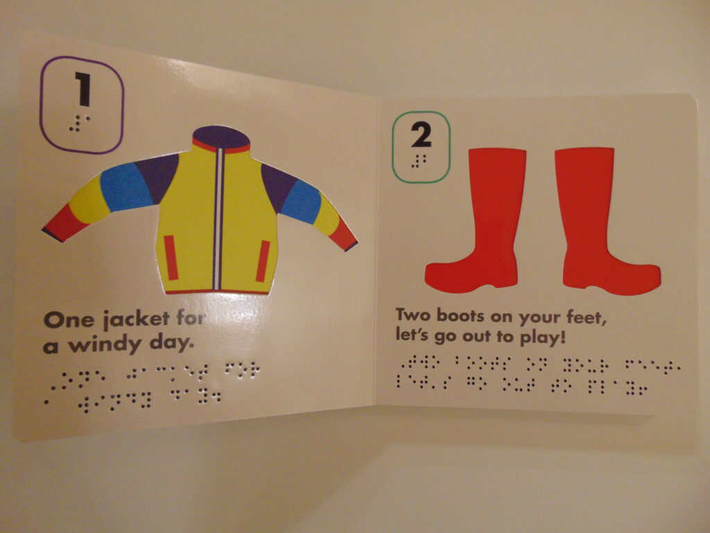 Image Description:  The page on the left has a print and braille “1” in the top left corner with a purple rectangle around it, a tactile (jacket material) image of a yellow jacket with purple and blue stripes and red trim is in the middle.  Underneath in print and braille is “One jacket for a windy day.”
The page on the right has a print and braille “2” with a green rectangle around it, a tactile image of slick red rainboots is in the center, underneath in print and braille is “Two boots on your feet, let’s go out to play!”